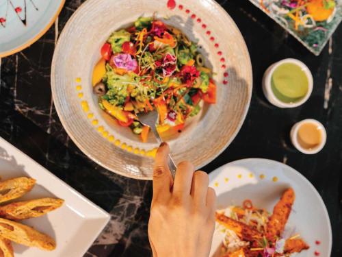 a table with two plates of food and a person eating a salad at Sunday Resort & Spa Manesar Gurugram in Gurgaon