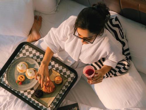 a woman sitting on a bed with a tray of food at Sunday Resort & Spa Manesar Gurugram in Gurgaon