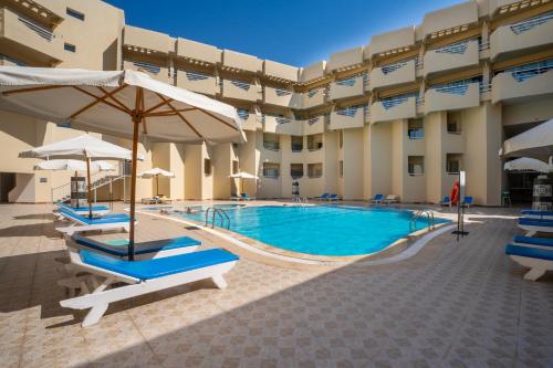 a swimming pool with chairs and umbrellas in front of a building at Seven Seas Jolie Bay - Ultra All Inclusive in Hurghada