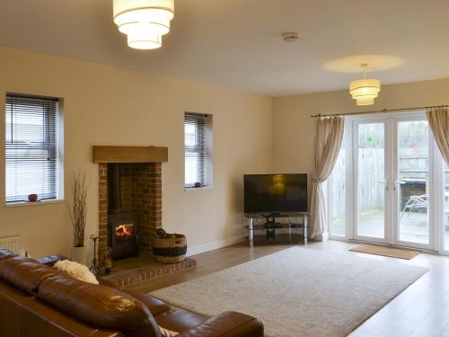 ein Wohnzimmer mit einem Sofa, einem TV und einem Kamin in der Unterkunft Abbey Cottage in Longhirst