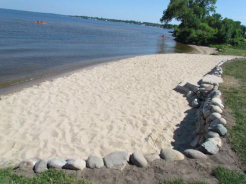 a beach with rocks on the shore of the water at Lakeside Resort & Conference Center in Houghton Lake