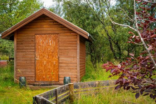 a small wooden cabin with a door in the grass at Riverside Cabin - Hot Tub, Fishing and Relaxing Escape in Laugarvatn
