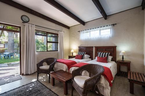 a bedroom with two beds and chairs and a window at Be My Guest Lodge in Bloubergstrand
