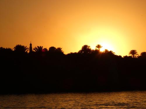 a sunset over the water with a tower in the background at Felucca, welcome sailing in Aswan