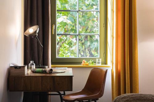 a desk with a lamp and a chair in front of a window at Contact Hôtels Le Savigny & Spa in Blacé