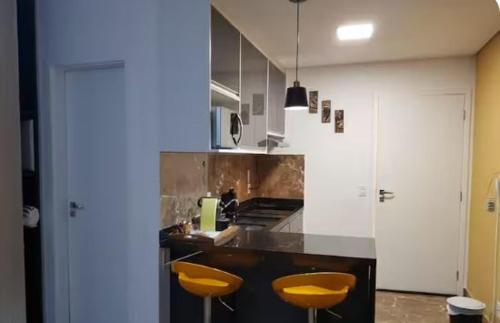 a kitchen with two yellow stools and a counter at Flat Novo1 - Café, Cama Queen, Ar, Estac e Internet in Barueri