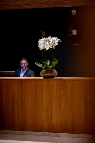 a man sitting behind a counter with a vase of flowers at Hotel Dom Carlos Park in Lisbon