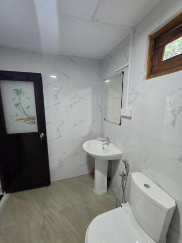 a white bathroom with a toilet and a sink at Veenora Wild - Guest House in Anuradhapura