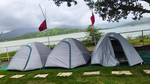 two tents sitting on the grass next to a river at Mid Night Camping- Pawna Lake in Kolvan