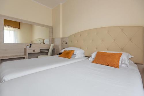 a bedroom with a large white bed with two orange pillows at Hotel Castello Artemide Congressi in Castel San Pietro Terme