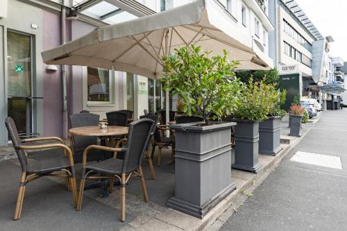 a table with chairs and an umbrella on a sidewalk at Garner Hotel Aschaffenburg Post by IHG in Aschaffenburg
