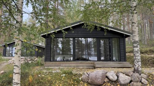 a black cabin in the woods with trees at LakeLodge Kiehinen & Igloos in Rovaniemi