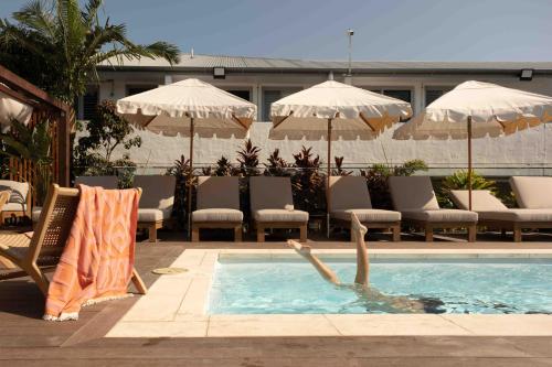 a person swimming in a pool with chairs and umbrellas at Drifter Byron Bay in Byron Bay
