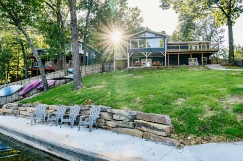 a house with chairs on a lawn next to the water at Heron House-ON Lake Avalon - near MTB in Bella Vista
