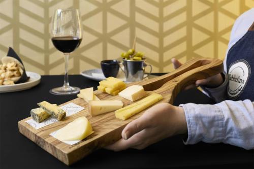 a person holding a cutting board with cheese and a glass of wine at NH Madrid Nacional in Madrid