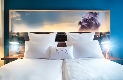 a bed with white pillows and a painting on the wall at NYX Hotel Mannheim by Leonardo Hotels in Mannheim