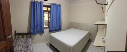 サンタ・テレサにあるRecanto MÃEFILHAのベッド1台、青いカーテン付きの窓が備わる客室です。