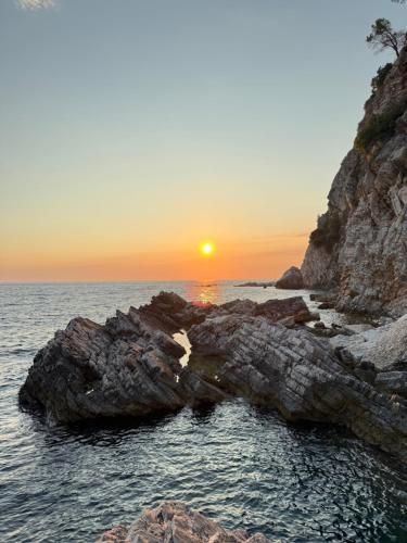 a sunset over the ocean with rocks in the water at Apartman Dunja Bečići in Becici