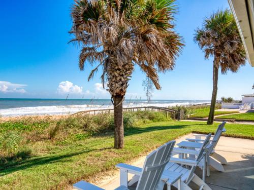 a row of chairs and a palm tree next to the beach at Sunrise Cottage by the Sea in Ormond-by-the-Sea