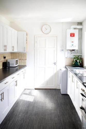 a kitchen with white cabinets and a clock on the door at Beautiful 5Bedroom House - Contractors and Family near the Molineux stadium in Wolverhampton