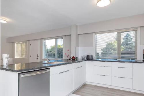 a white kitchen with white cabinets and windows at Modern Spacious Ocean-view Suite with Private Ent in West Vancouver