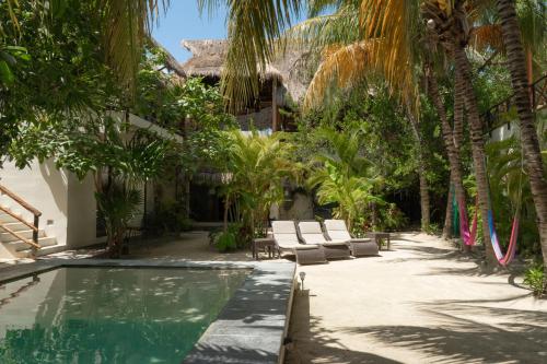 a resort pool with lounge chairs and palm trees at Hotel Boutique La Puerta Azul Beachfront - Adults Only in Holbox Island