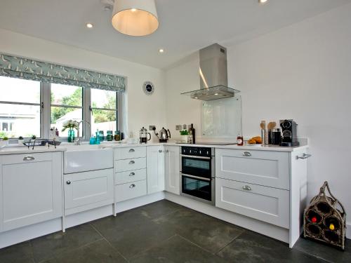 a kitchen with white cabinets and a sink and a stove at Oakwood in Saint Endellion