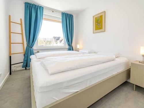 two beds in a white bedroom with blue curtains at One-bedroom apartment in Westerland (Sylt)