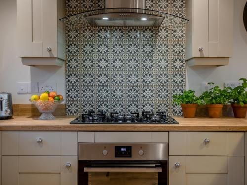 a kitchen with a stove and a tile wall at Wisteria House in Henstead
