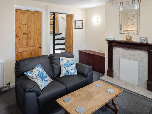 a living room with a black leather couch and a fireplace at Happy Days in Whitby