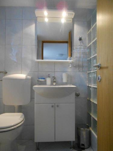 a white bathroom with a toilet and a sink at Studio apartman Kornelija in Lumbarda