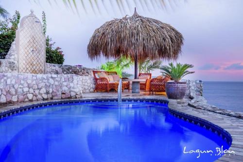 a swimming pool with an umbrella and chairs and the ocean at Oceanfront apartments 18 & 19 - Lagun Blou Dive & Beach Resort, Curaçao in Lagun