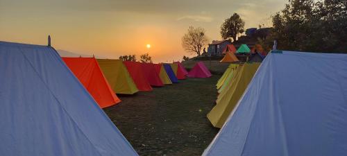 a row of colored tents with the sunset in the background at Nag Tibba Trek - Three Sixty Views in Miānī