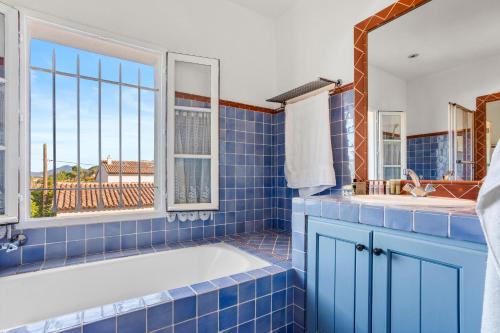 Un baño con azulejos azules, bañera y ventana. en Maison Ferienhaus Grillons, en Saint-Tropez