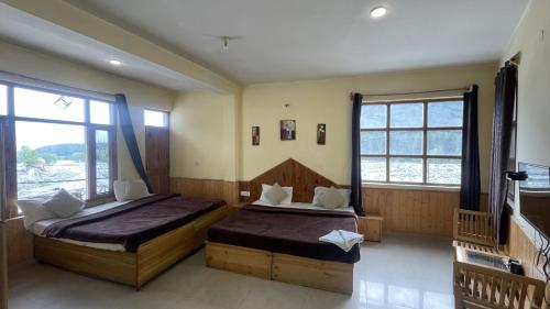 two beds in a room with two windows at Singh Saab Rooms & Cafe in Manāli
