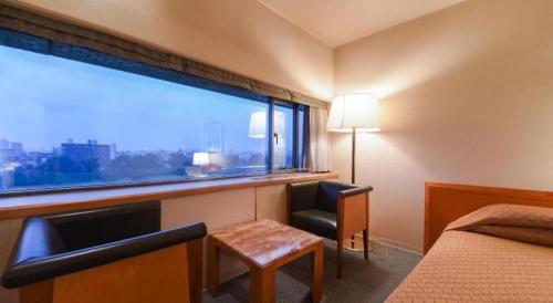 a hotel room with a window and a bed and a chair at Gunma Royal Hotel in Maebashi