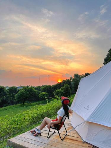 a woman sitting in a chair next to a white tent at Sunny Camping Sóc Sơn in Sóc Sơn