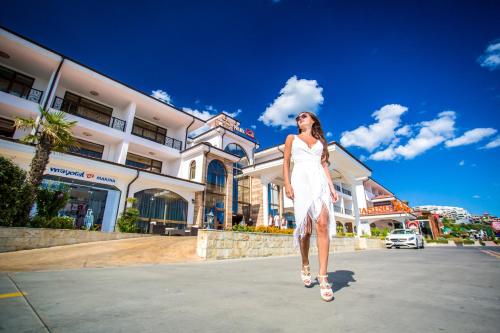 a woman in a white dress walking down a street at Hotel Palace Marina Dinevi in Sveti Vlas