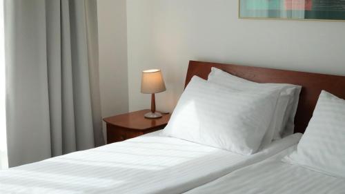 a bed with white sheets and a table with a lamp at BEST BALTIC Kaunas in Kaunas