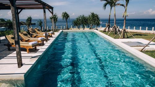 a swimming pool with lounge chairs and the ocean at Naluna Lembongan in Nusa Lembongan