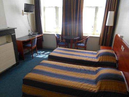 イーペルにあるHotel Old Tomのベッド2台とデスクが備わるホテルルームです。