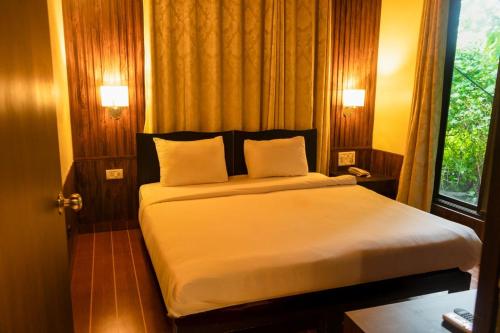 a bedroom with a bed with white sheets and a window at Silvanus Forest Retreat, Alibaug in Alibaug