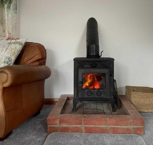 a stove in the corner of a room with a couch at Rural Farm Cottage nr Canterbury - logburner, parking, 2bed and 2bath -idyllic setting in Stelling