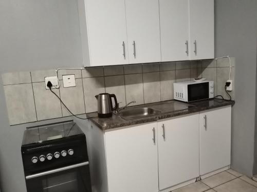 una cucina con mobili bianchi, un lavello e un microonde di Capital Park entire rental unit a Pretoria