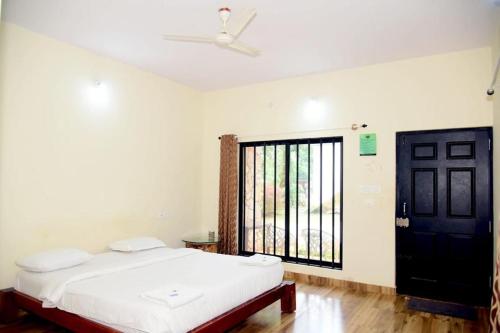 a bedroom with a white bed and a black door at Shola Vibes Homestay in Chikmagalūr