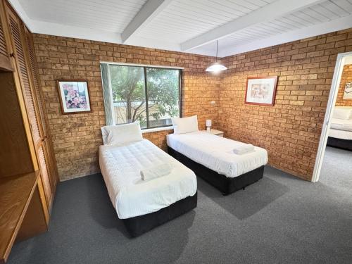 a room with two beds and a brick wall at Golden Sands Motor Inn in Forster