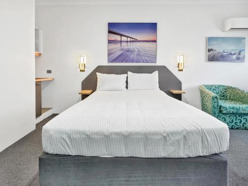 a bedroom with a white bed and a blue chair at Golden Sands Motor Inn in Forster