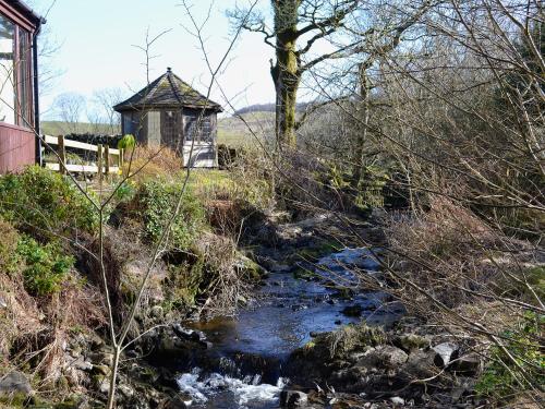 a stream with a small building next to a river at Arkland Mill in Corsock