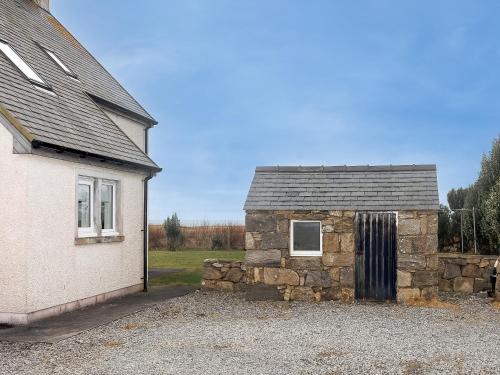 a stone building next to a house with a window at Sealladh Na Mara in Pollachar