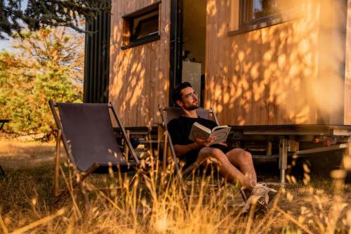 a man sitting at a table reading a book at Lodge en Nature - 30 min Saint-Emilion - Salle de bain à l'italienne in Mouliets-et-Villemartin